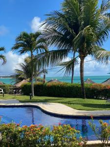a swimming pool with palm trees and the ocean at Tamandaré Holiday Flat Beira-Mar Apartamento 107 in Tamandaré