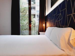 1 dormitorio con cama blanca y ventana en Hostal Laia by gaiarooms en Barcelona