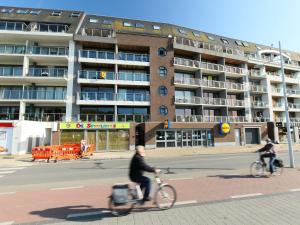 two people riding bikes down a street in front of a building at Apartment Residentie Albatros by Interhome in Bredene