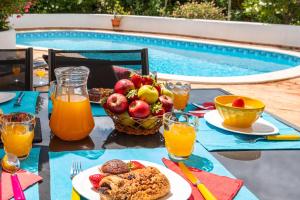a table with a breakfast of fruit and juice next to a pool at Villa Sunshine by Algarve Vacation in Armação de Pêra