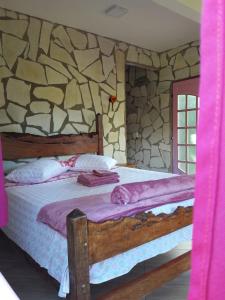 1 dormitorio con cama de madera y pared de piedra en Repouso Sol, en São Thomé das Letras
