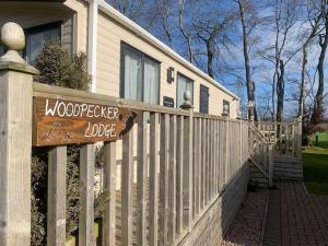 a house with a wooden sign on a fence at Woodpecker lodge, Camelot Holiday Park, CA6 5SZ in Carlisle