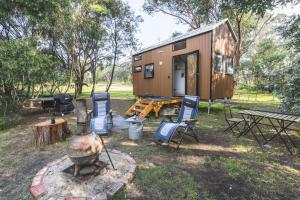 a tiny house with chairs and a table and a grill at Tiny Hideaway at Cloverhills in Newham