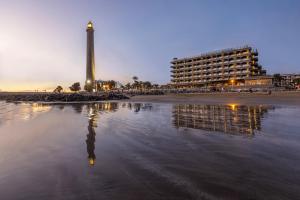a beach with a lighthouse and a building and a building at Hotel Faro, a Lopesan Collection Hotel - Adults Only in Maspalomas