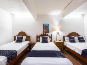 two twin beds in a room with white walls at Capital O Posada La Casa De La Tia, Oaxaca in Oaxaca City