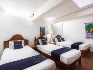 3 Betten in einem Zimmer mit weißen Wänden in der Unterkunft Capital O Posada La Casa De La Tia, Oaxaca in Oaxaca de Juárez