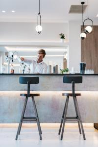 a man standing behind a bar with two bar stools at Tesoro Hotel Zakynthos in Tsilivi
