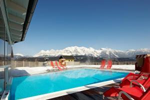 uma piscina com cadeiras vermelhas e montanhas cobertas de neve em Hotel Moser em Schladming