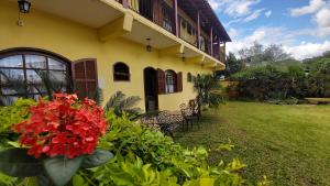 une maison jaune avec des fleurs rouges dans une cour dans l'établissement Pousada da Josi - Tiradentes, à Tiradentes