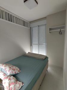 um pequeno quarto com uma cama e uma janela em Apartamento Pé na Areia em Florianópolis