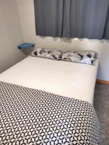 ein Bett mit einer schwarzen und weißen Bettdecke und einem Fenster in der Unterkunft Beach Haven Caravan Park in San Remo