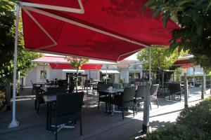 a patio with tables and chairs under a red umbrella at The Originals City, Hôtel du Phare, Bordeaux Mérignac (Inter-Hotel) in Mérignac