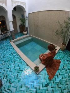 a woman sitting on the floor next to a swimming pool at Riad Dollar Des Sables & Spa in Marrakesh