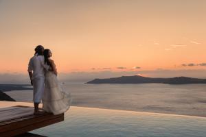 a bride and groom standing on a balcony overlooking the ocean at West East Suites in Imerovigli