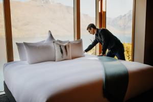 mężczyzna stojący obok łóżka w pokoju hotelowym w obiekcie Azur Lodge w mieście Queenstown