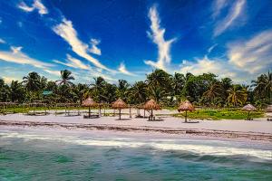 a beach with some straw umbrellas and the water at Hacienda Antigua Villa, 50m from sandy Beach in El Cuyo