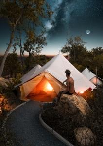 拉威海灘的住宿－Roost Glamping - SHA Certified，坐在帐篷旁边的岩石上的人