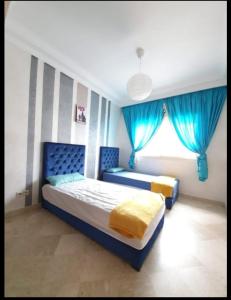 a bedroom with two beds with blue curtains and a window at Résidence jnane California in Casablanca