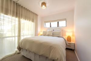 a white bedroom with a bed and a window at Bach 14 - Stay Waiheke in Blackpool