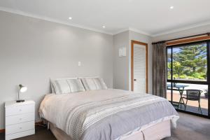 a white bedroom with a bed and a balcony at Upepo - The Garden Room - Cape Foulwind Studio in Cape Foulwind