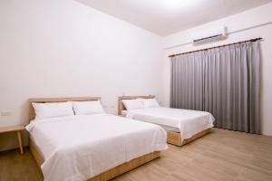 two beds in a room with white walls and wood floors at 澎湖逸軒居民宿 in Huxi
