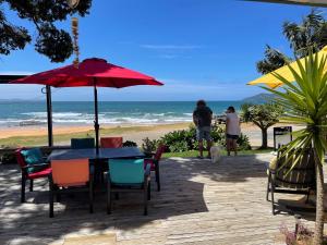 a table with chairs and an umbrella on the beach at Driftwood Beachfront Accommodation, Cable Bay, Owhetu in Coopers Beach