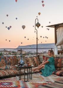 una mujer sentada en un sofá viendo globos de aire caliente en Hera Cave Suites, en Göreme