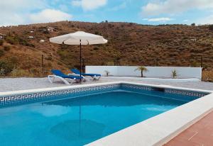 a swimming pool with an umbrella and two chairs and a table and an umbrella at Casa Verdejo in Cómpeta