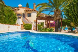 a swimming pool in front of a house with a palm tree at Villa Erik - PlusHolidays in Calpe
