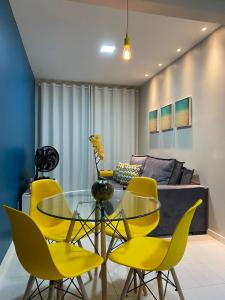 uma sala de jantar com uma mesa de vidro e cadeiras amarelas em Muro Alto Condomínio Clube Apt 316 em Porto de Galinhas