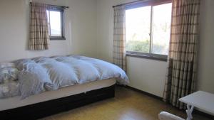 a bedroom with a bed with a blue comforter and two windows at Ken House Osaka in Takatuki