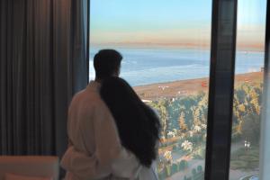 MiraMar Luxury Residences في باتومي: امرأة تطل من النافذة على المحيط