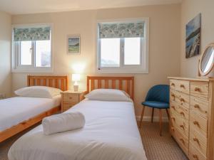 a bedroom with two beds and a blue chair at 48 Glan Y Mor in Fairbourne