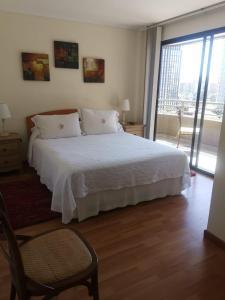1 dormitorio con 1 cama blanca y 1 silla en RoomApart Escuela Militar, en Santiago