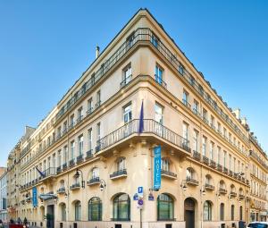 a large tan building with a blue sign on it at Hotel Vacances Bleues Provinces Opera in Paris