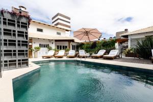 a swimming pool with chairs and an umbrella next to a building at Villa d'Ozio Hotel e Cucina in Itajaí