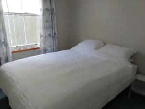 uma cama branca num quarto com uma janela em Milton Cottage em Napier