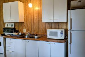 eine Küche mit weißen Schränken, einer Spüle und einer Mikrowelle in der Unterkunft Trendy, Mid-Century Styled Yellow Cottage on Sand Beach in Commanda