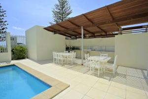 um pátio com uma mesa e cadeiras e uma piscina em Ground Floor Luxury Oceanfront Apartment em Bargara