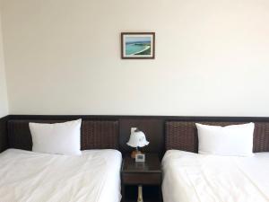 two beds with white sheets and a table with a lamp at Pine Shima Resort Coral Fish in Ibaruma