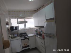 eine kleine Küche mit weißen Schränken und einem Kühlschrank in der Unterkunft Apto a 25 metros areia PITANGUEIRAS Vista mar 4 quartos 3 banheiros 1 vaga carro Serviço de praia in Guarujá