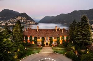 a house on the lake with mountains in the background at Villa Principe Leopoldo - Ticino Hotels Group in Lugano