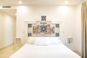 un lit blanc dans une chambre avec un mur carrelé dans l'établissement Posada Boutique El Gallo Morón, à Morón de la Frontera