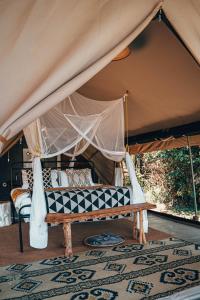 a canopy bed with a bench in a tent at Emboo River Camp in Talek