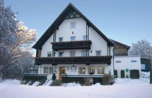 une grande maison blanche avec un toit en gambrel dans la neige dans l'établissement Gasthaus zur Traube, à Winterrieden