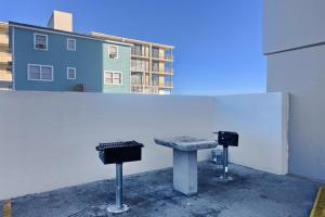 a bench and two trash cans next to a white wall at Gulf Tower 14W in Gulf Shores