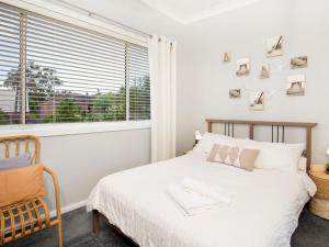a white bedroom with a bed and a window at Roskell Retreat Pet Friendly 5 Mins Walk to Beach in Callala Beach