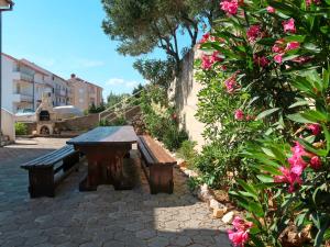 a wooden table and bench in a courtyard with pink flowers at Apartment Andrea - RAB100 by Interhome in Rab