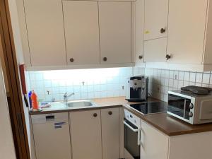 eine Küche mit weißen Schränken, einer Spüle und einer Mikrowelle in der Unterkunft Apartment Sunnmatt 128 by Interhome in Engelberg