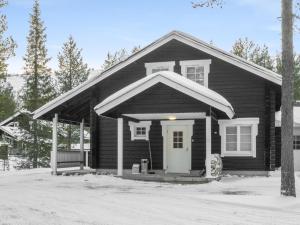 a black house with a white door in the snow at Holiday Home Rapsakka a by Interhome in Sirkka